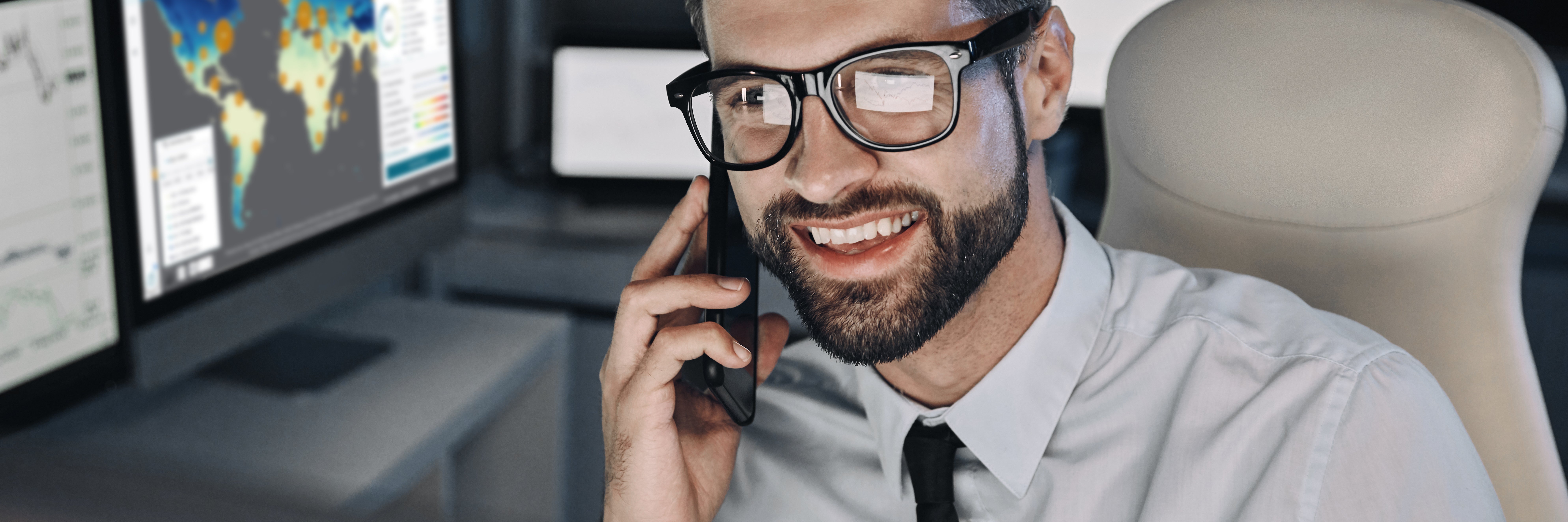 Smiling businessman talking on mobile phone and looking at computer screen in office