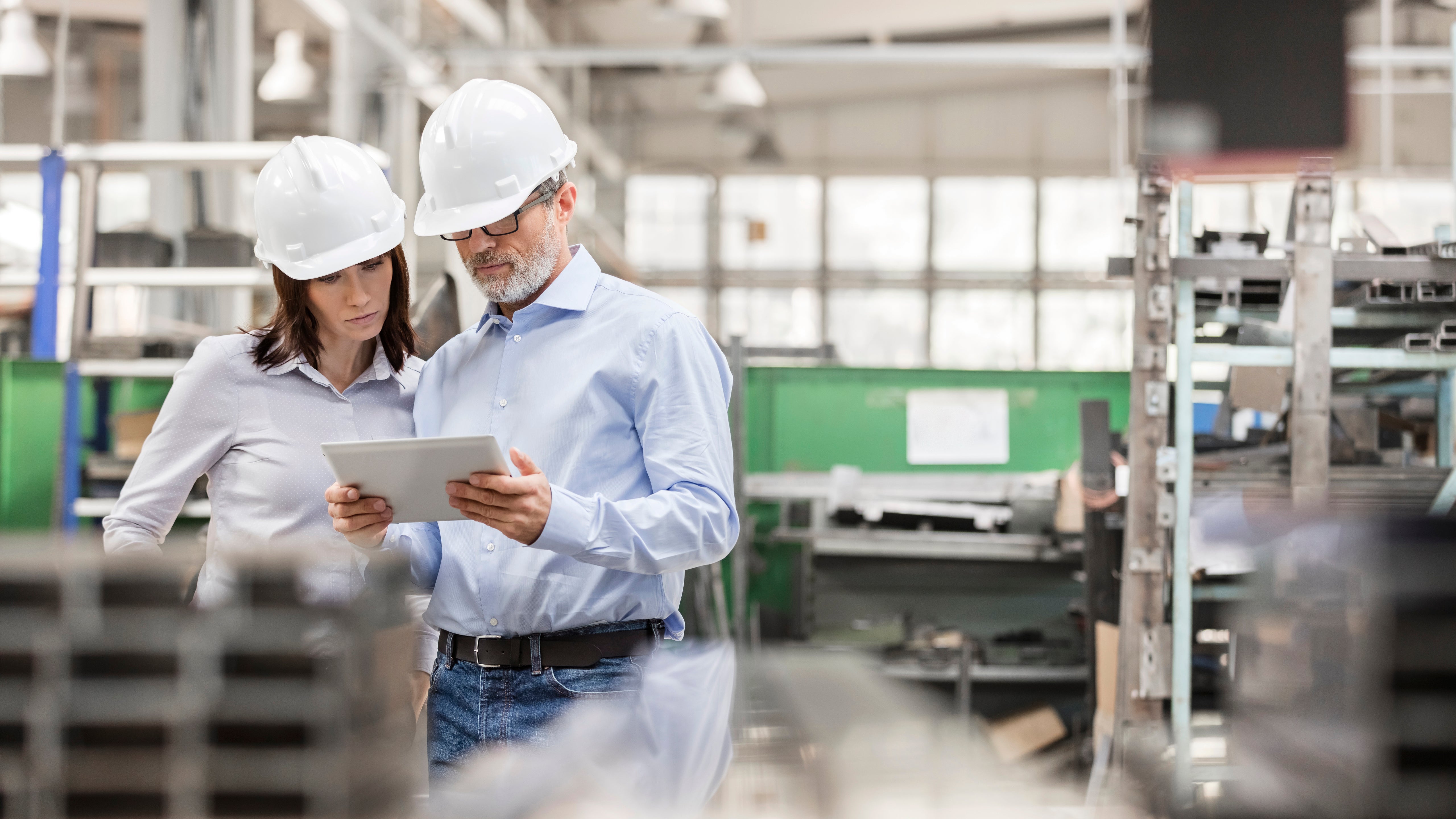 2 professionals wearing hard hats looking at tablet in industrial setting