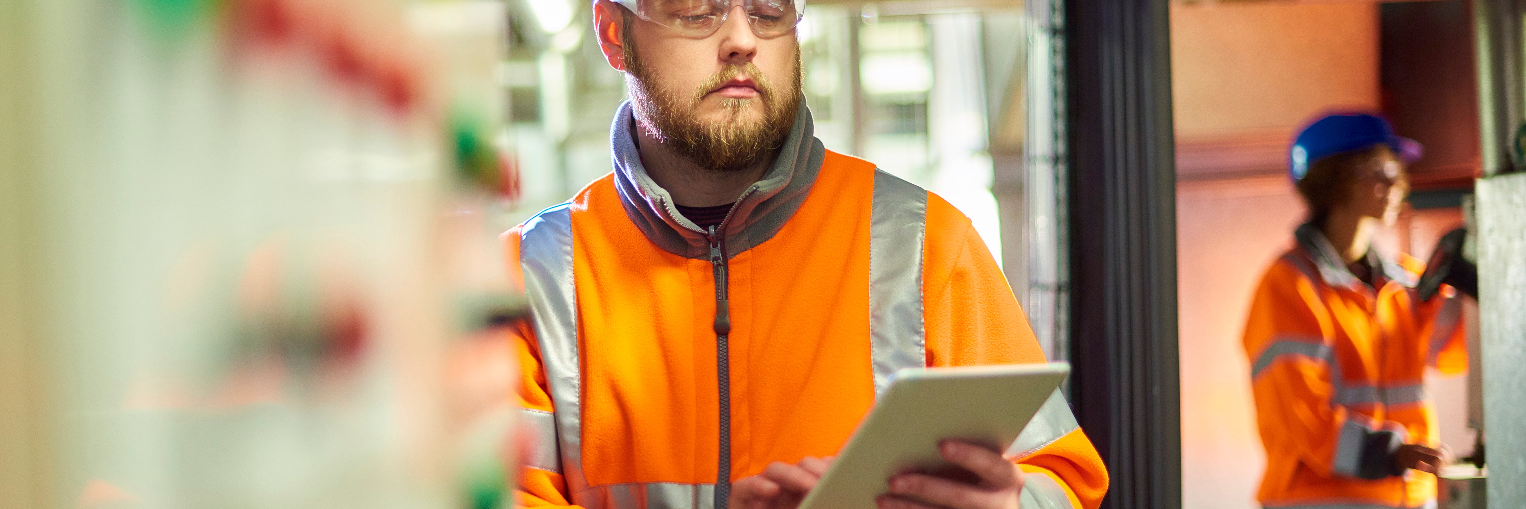 An industrial service engineer conducts a safety check of a control panel in a boiler room. He is wearing hi vis, hard hat, safety glasses and holding a digital tablet as he conducts a safety inspection.