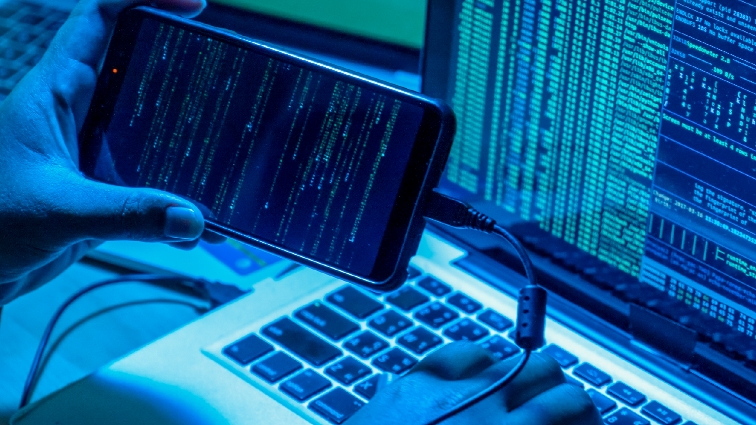 Un pirate informatique avec des ordinateurs et un téléphone intelligent dans une pièce sombre commettant un cyber-crime