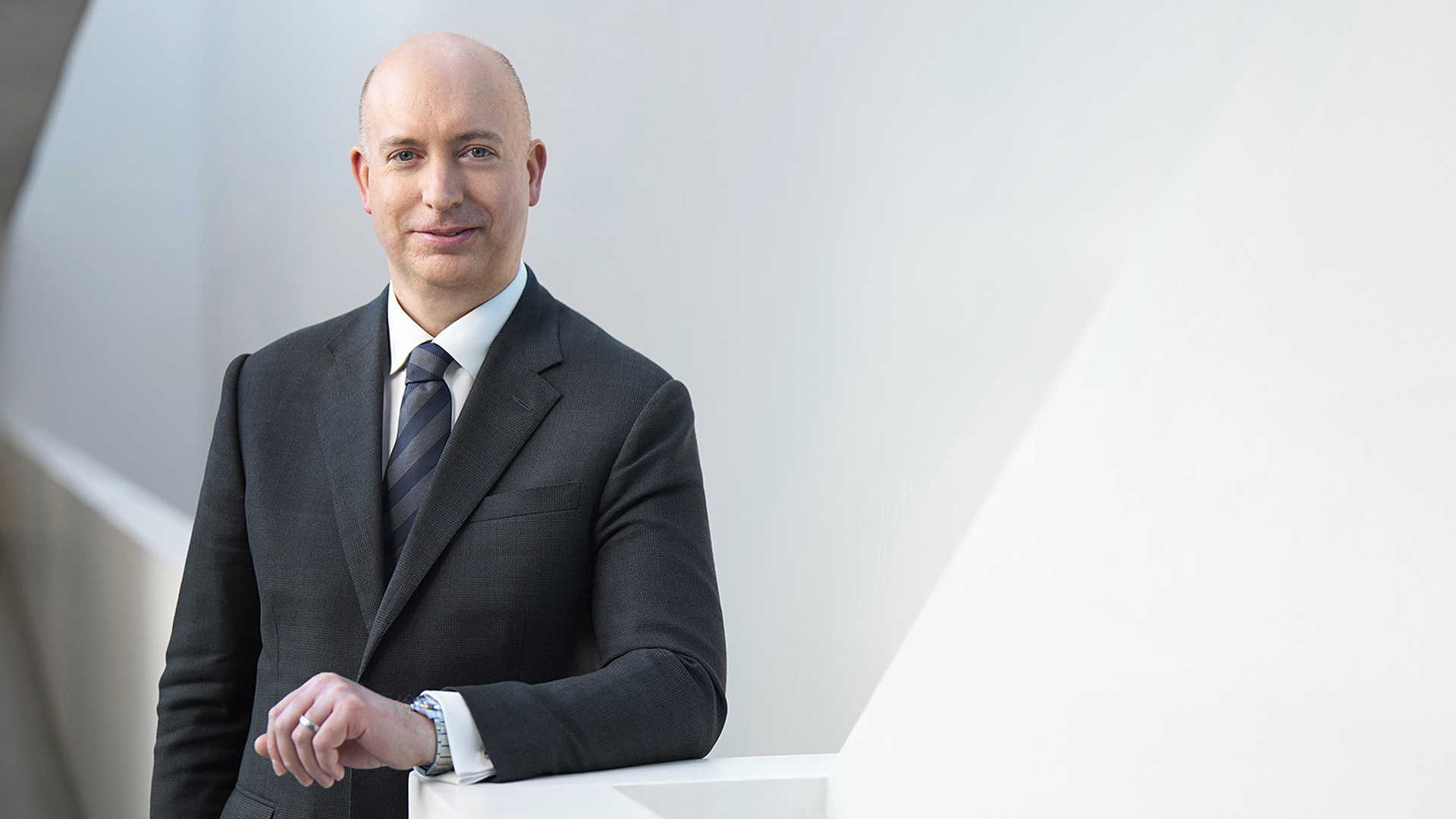 Ein Mann in einem Anzug steht an einer weißen Wand und hält seine Hand auf einer weißen Fläche.