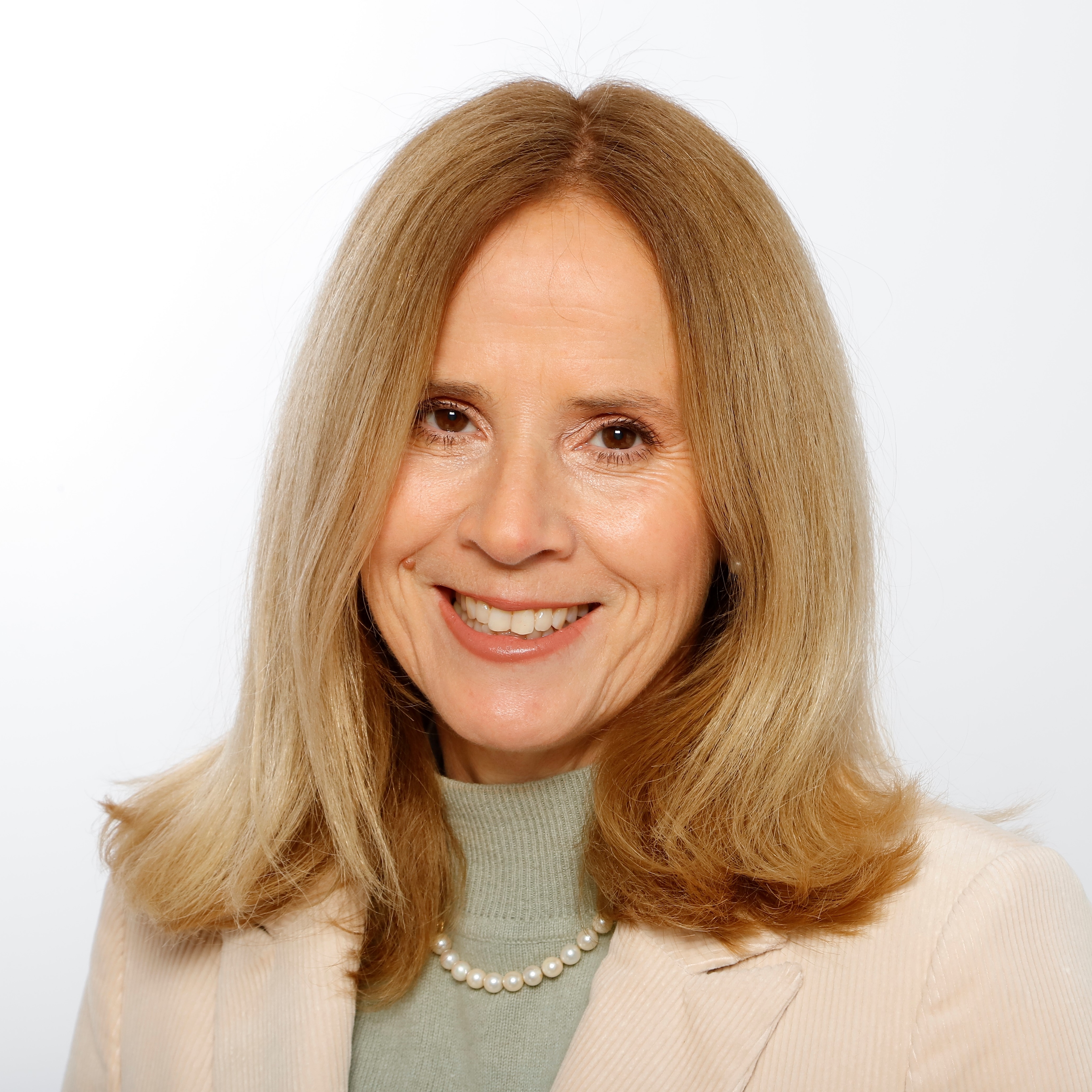 A woman with long, wavy blonde hair wearing a pearl necklace and a light-colored blazer against a white background.