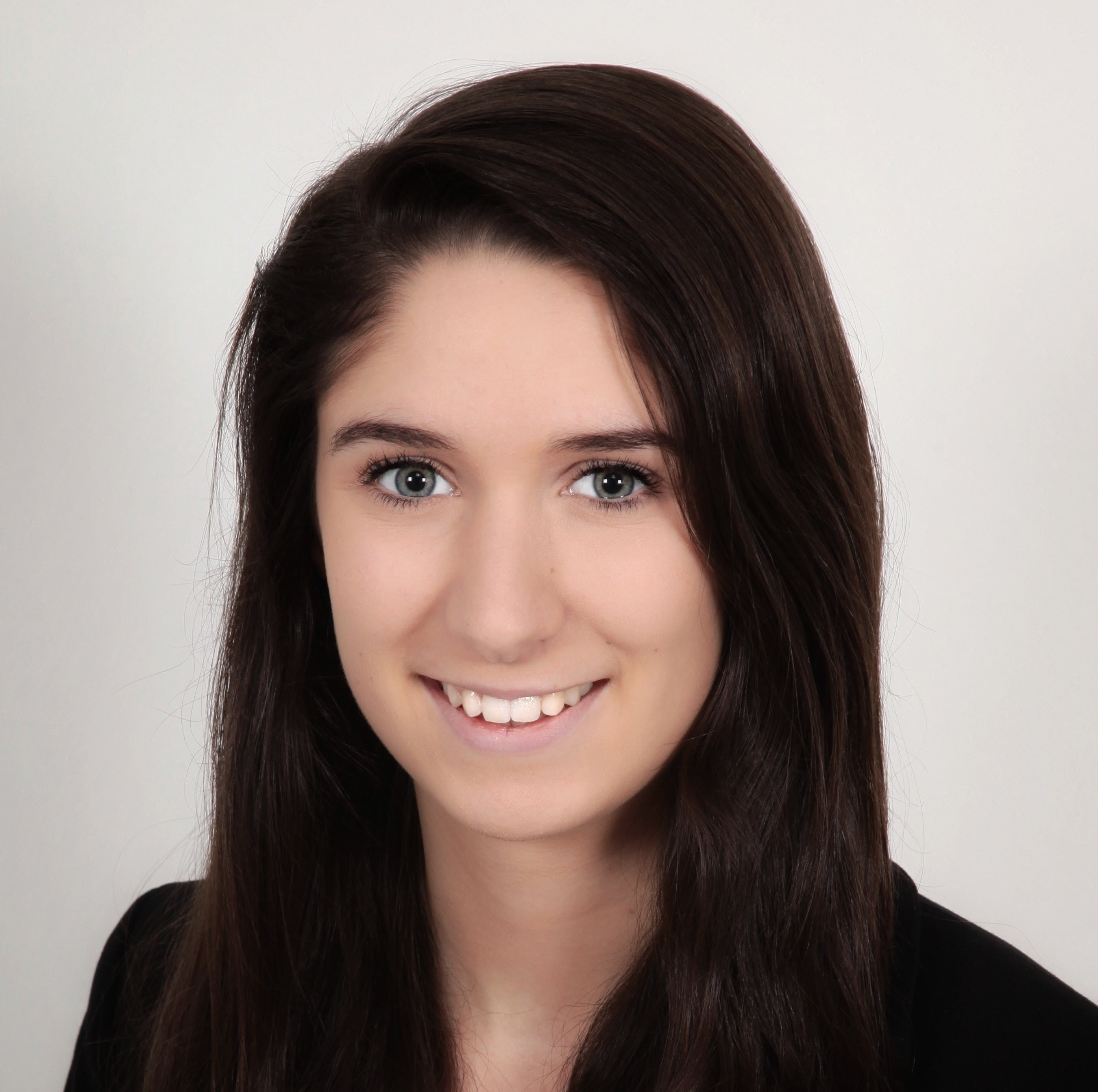 A young woman with long dark hair smiles at the camera, wearing a black jacket against a light background.