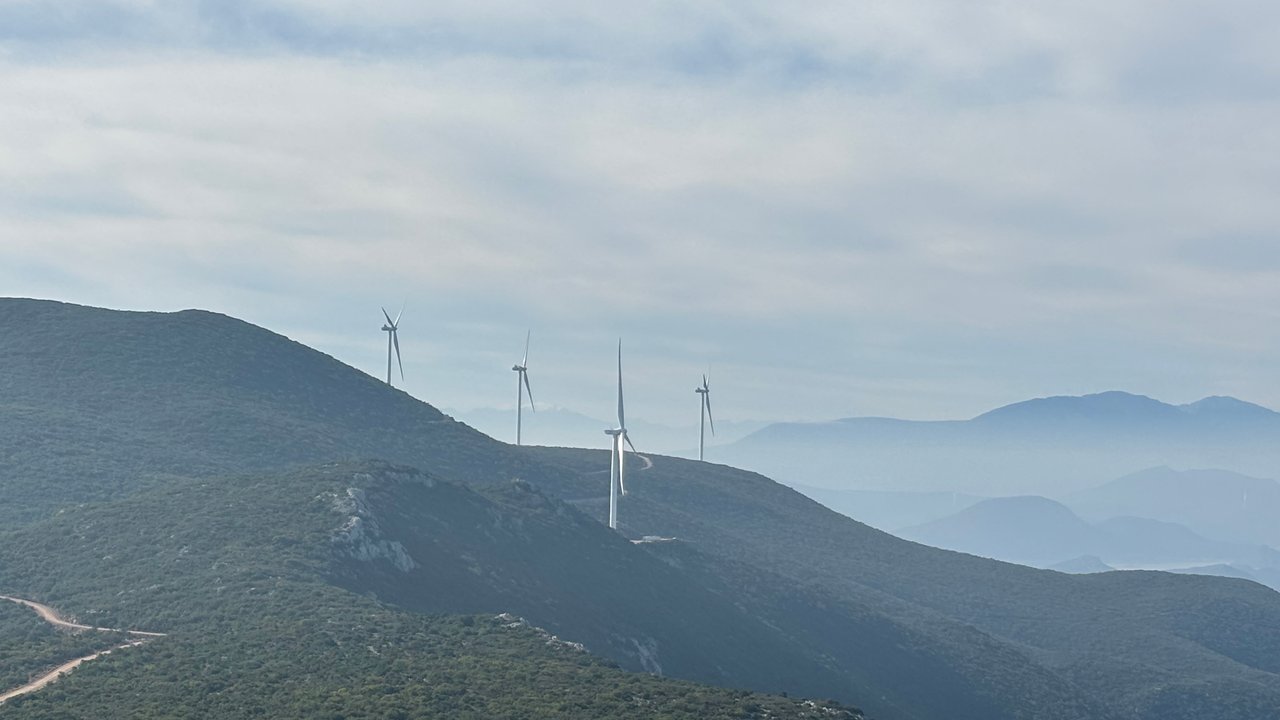 Windkraftanlagen stehen auf Hügeln in einer nebligen Landschaft mit sanften, grünen Bergen im Hintergrund.