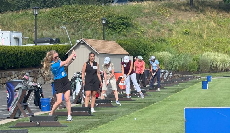 A group of women practicing golf swings at a driving range with various golf clubs and equipment.