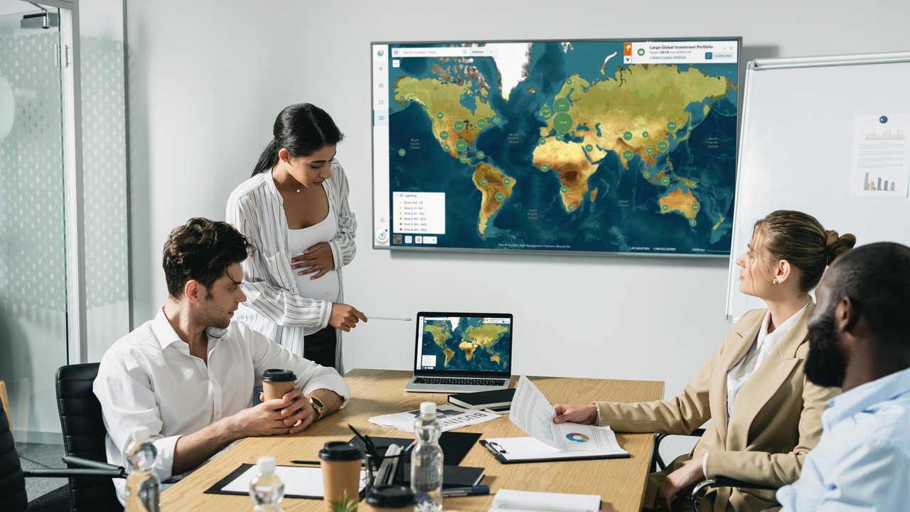 A group of four people in a meeting room with a laptop, documents, and drinks on a table.