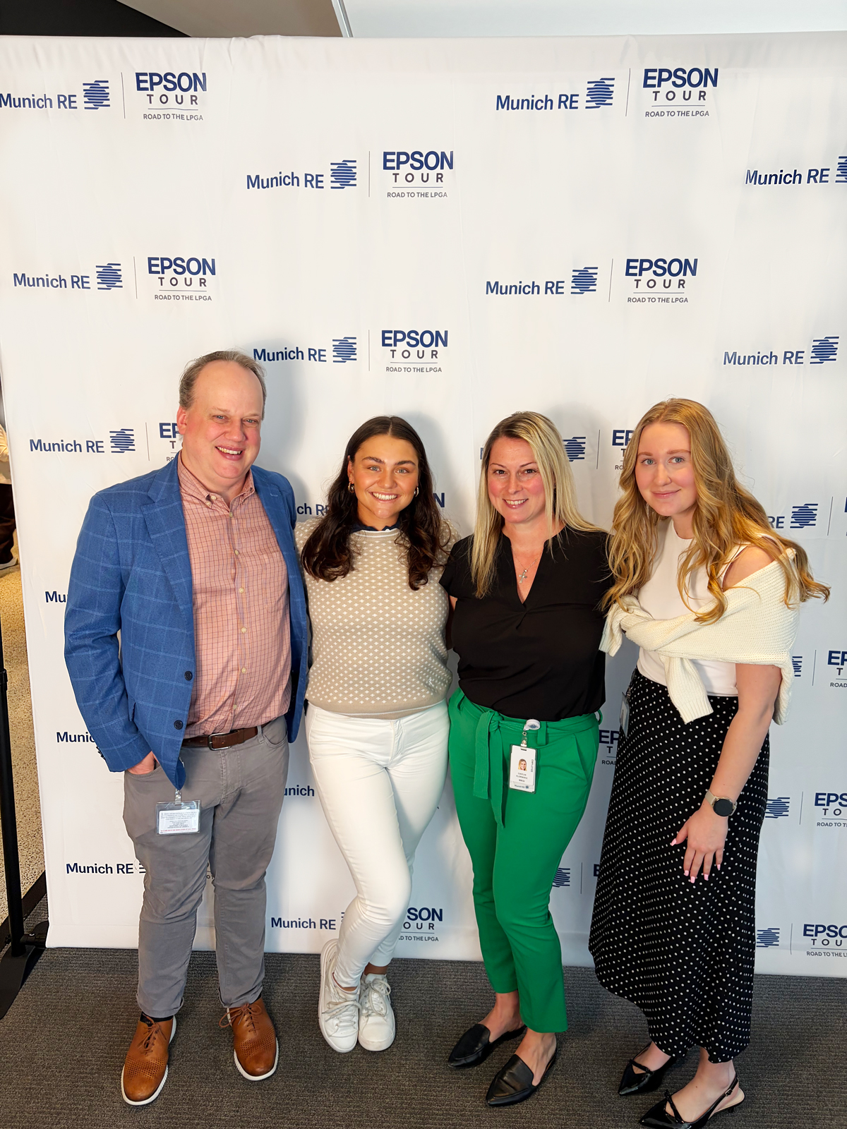 Four people pose together in front of a branded backdrop for the Epson Tour and Munich RE.