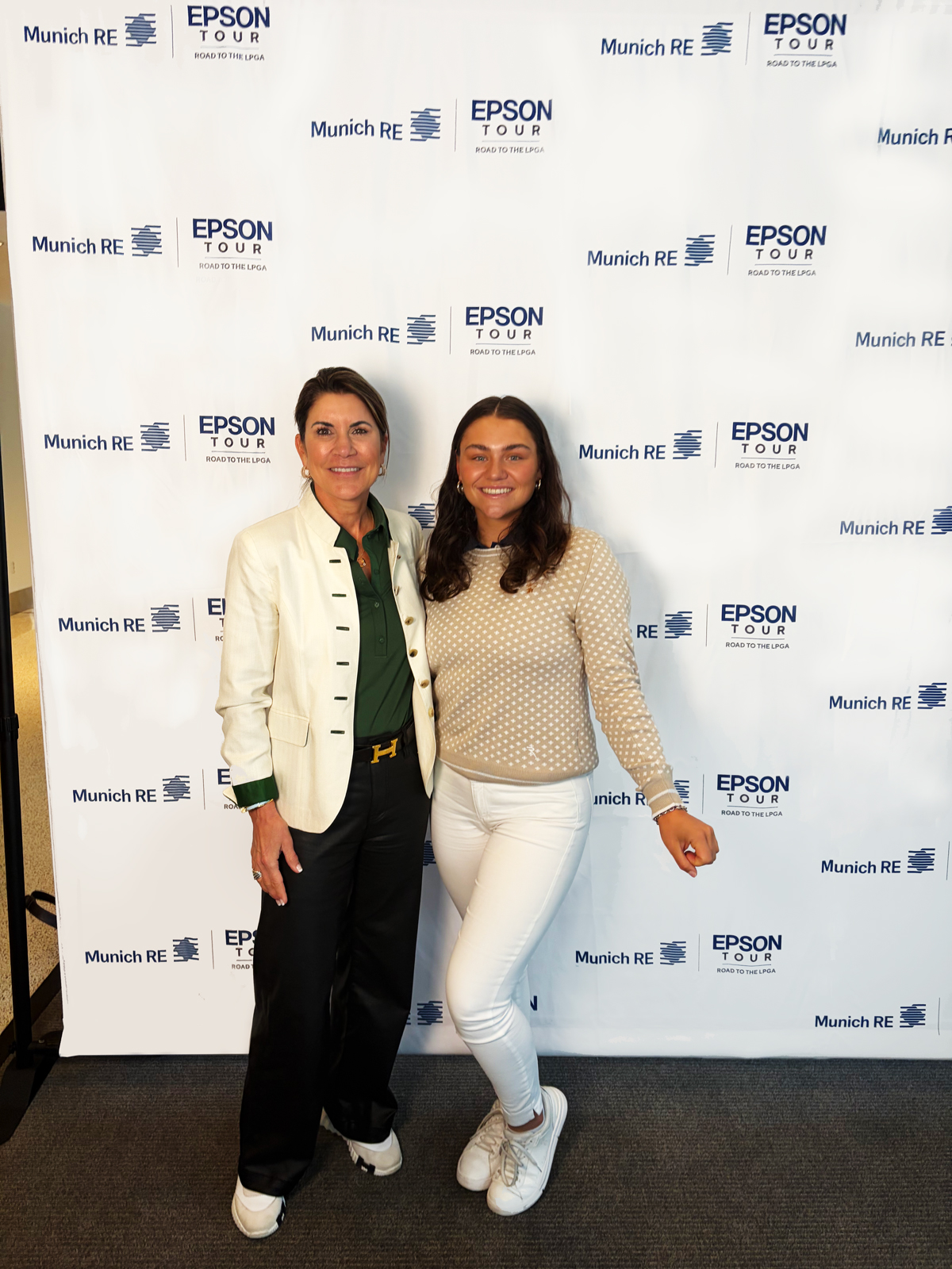 Two women pose together in front of a branded backdrop featuring logos for Epson Tour and Munich RE.