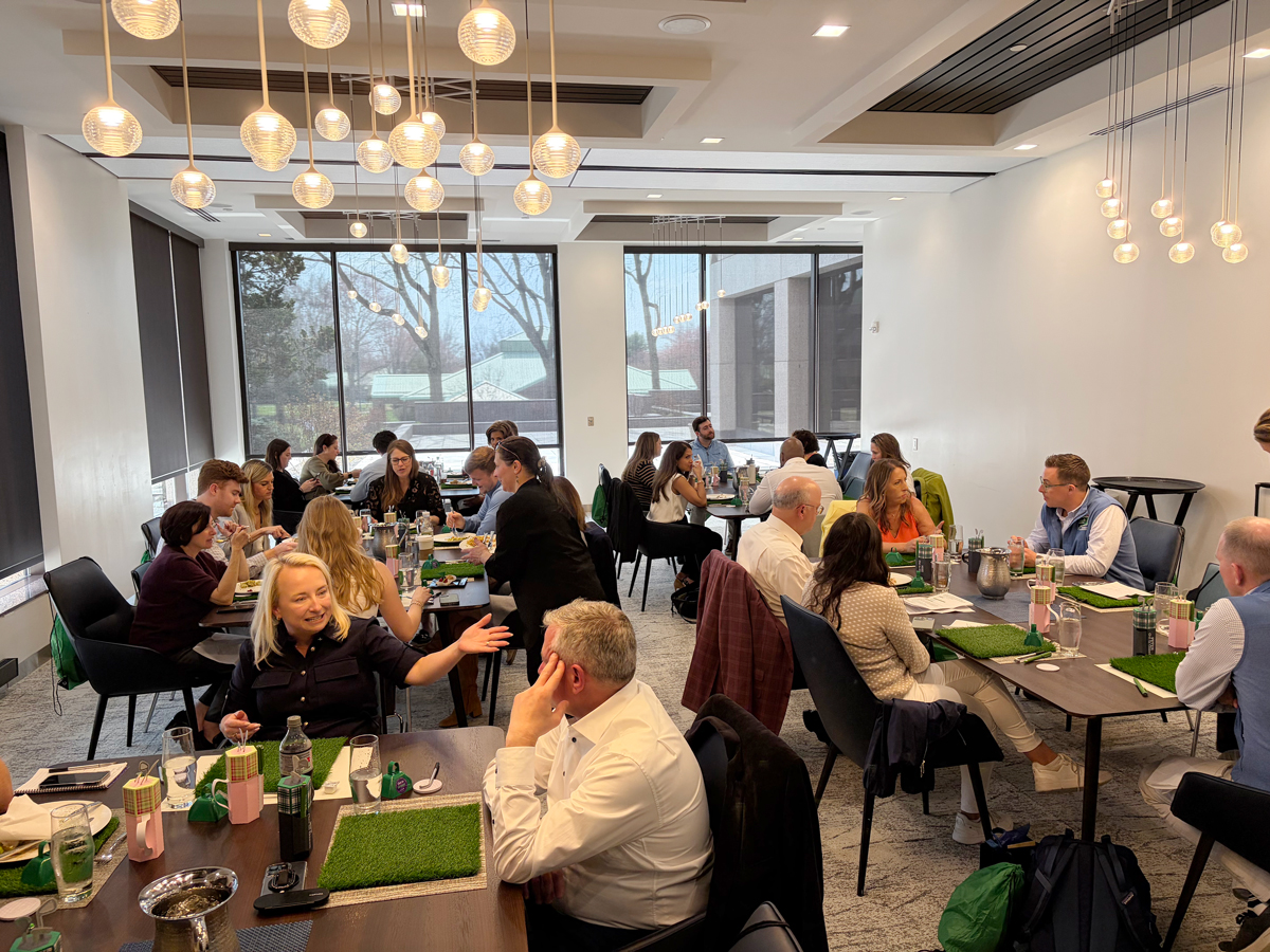 A group of people dining in a modern room with large windows and pendant lights, engaged in conversation.