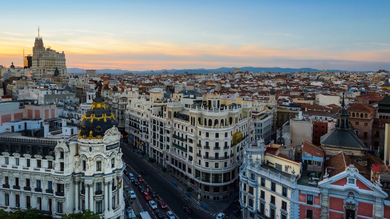 Aerial view of Madrid's skyline at sunset, featuring historic buildings and a busy street.