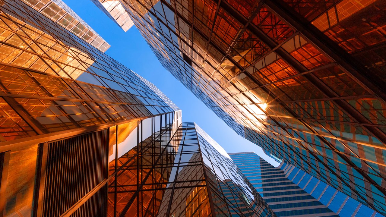 View of buildings from the street with lots of glass windows and a small strip of blue sky