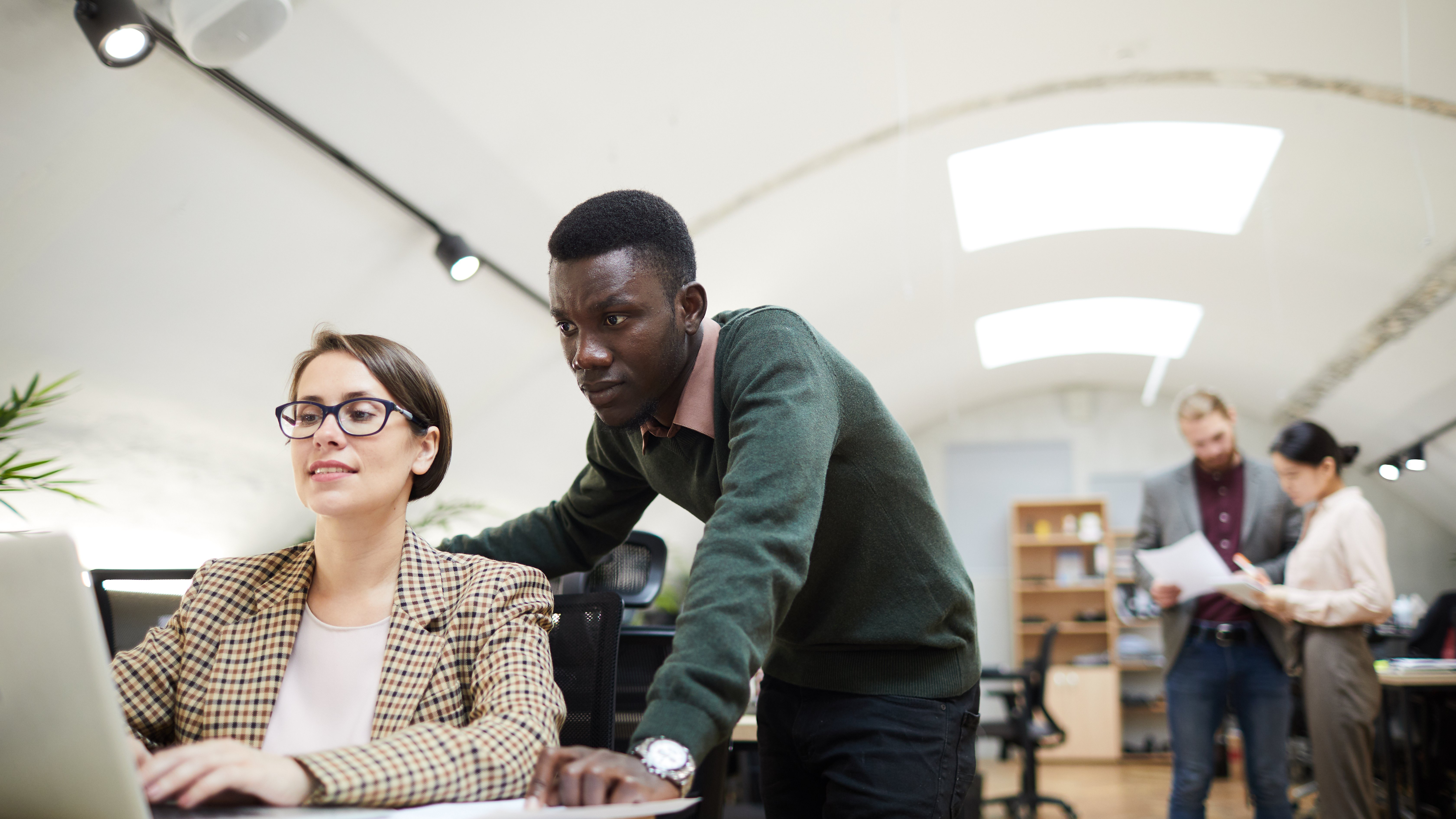 Portrait of young African businessman using laptop with female colleague while working in office, copy space