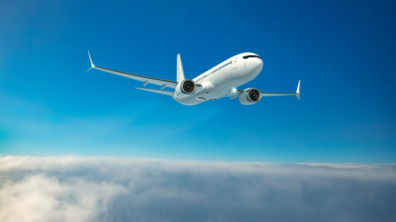 A white airplane flying above clouds against a clear blue sky.