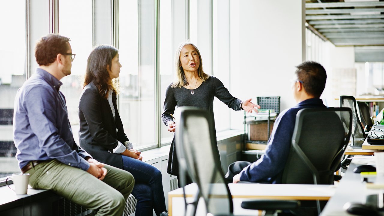 Mature businesswoman leading discussion during team meeting with coworkers in office
