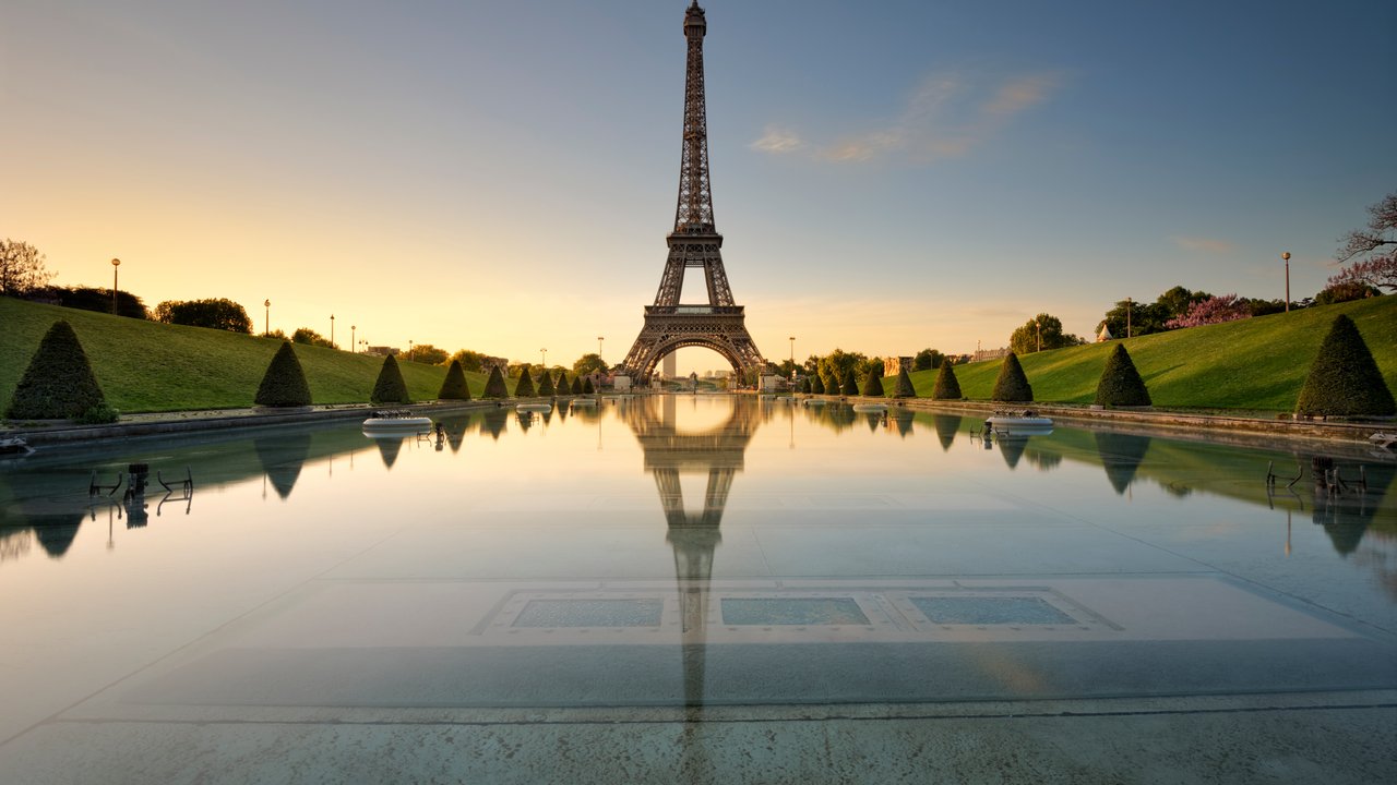 Eiffel Tower Reflected in Serene Water at Sunrise The Eiffel Tower stands tall over a reflective pool, surrounded by manicured lawns and trees at sunrise.