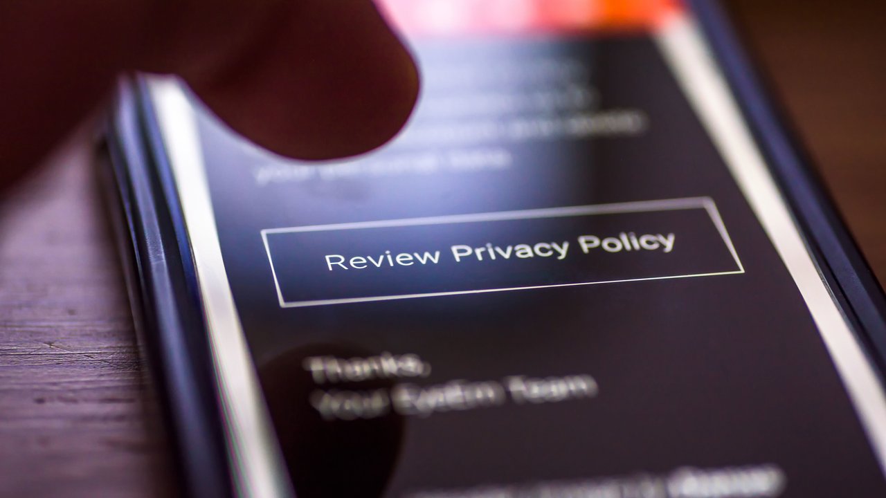 A finger hovers over a smartphone screen displaying a "Review Privacy Policy" button.