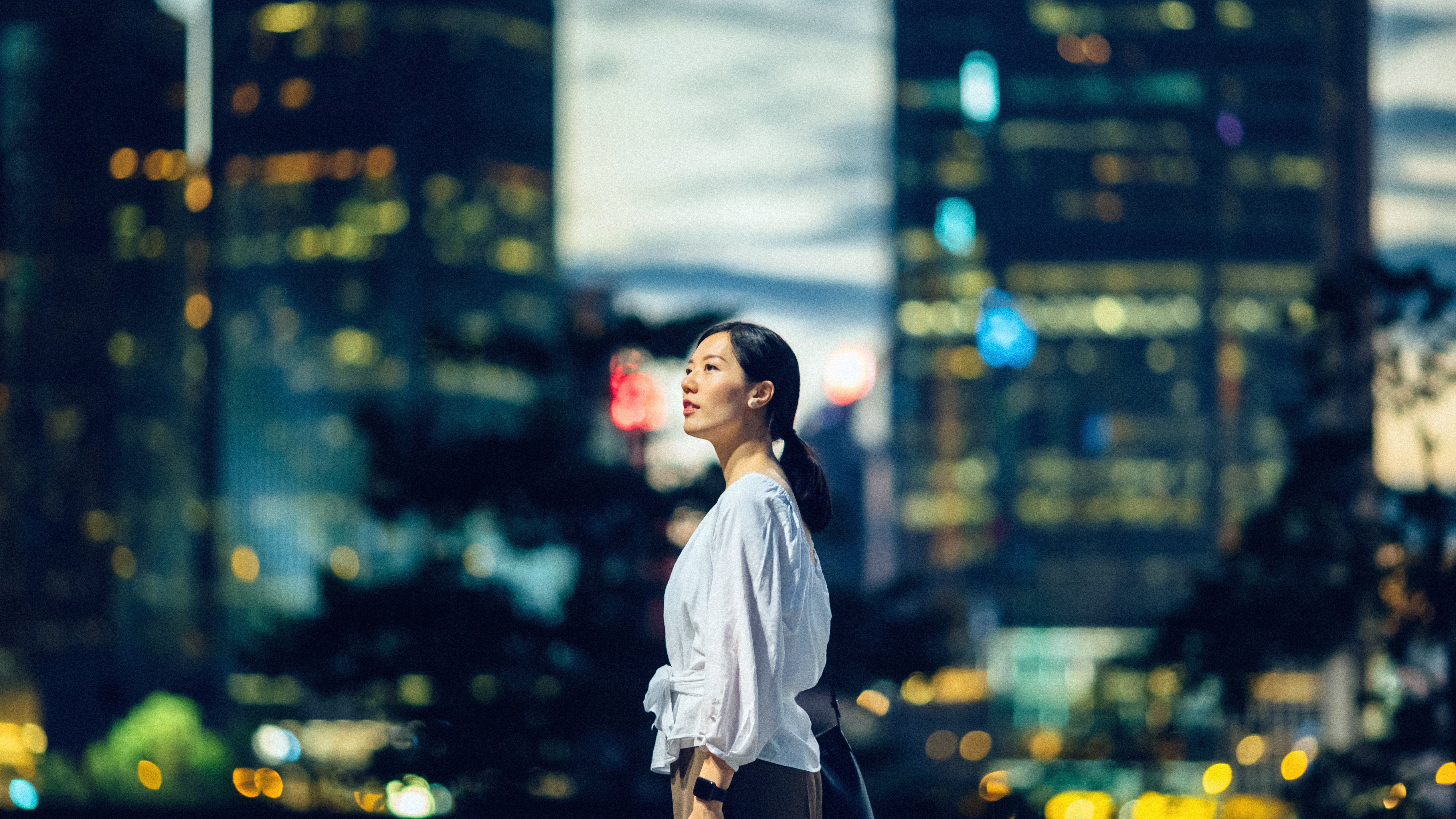 Confident young Asian woman standing against illuminated city buildings and thinking of her career path