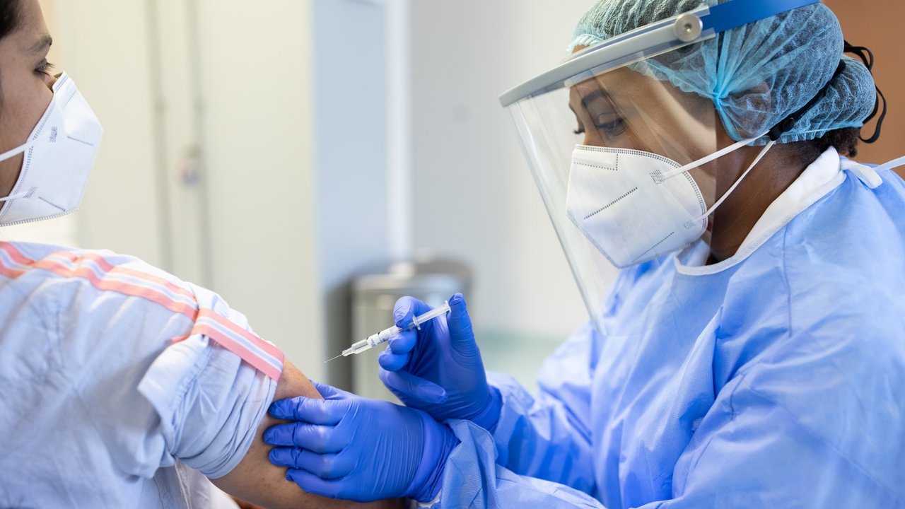 Doctor in personal protective equipment vaccinating a patient for COVID19