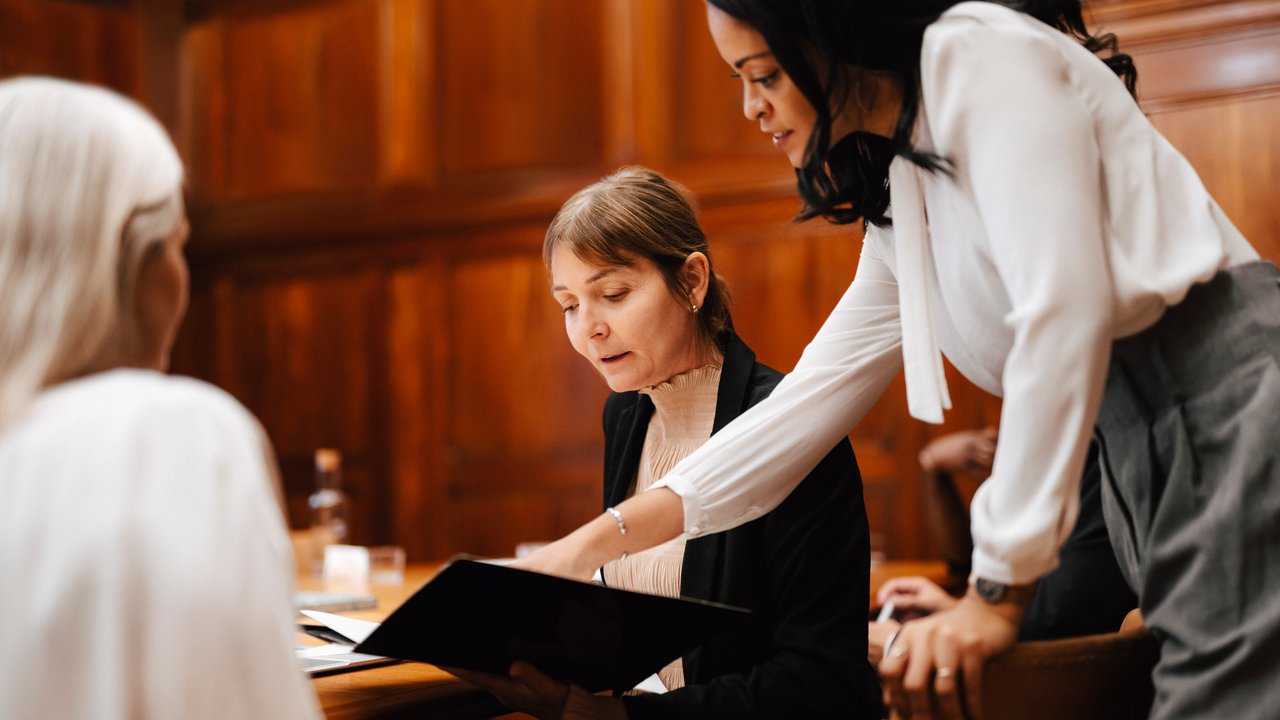 Women discuss document in wood-panelled room