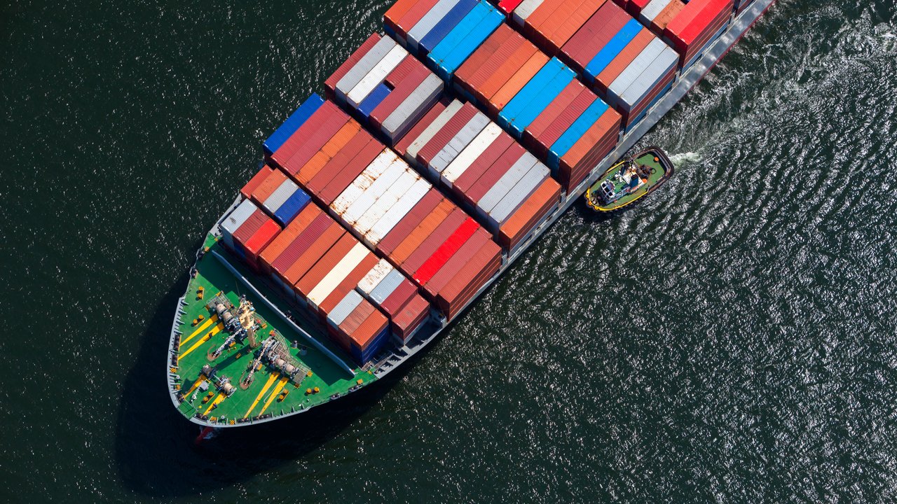 A tugboat attempting to guide a large container ship into port.