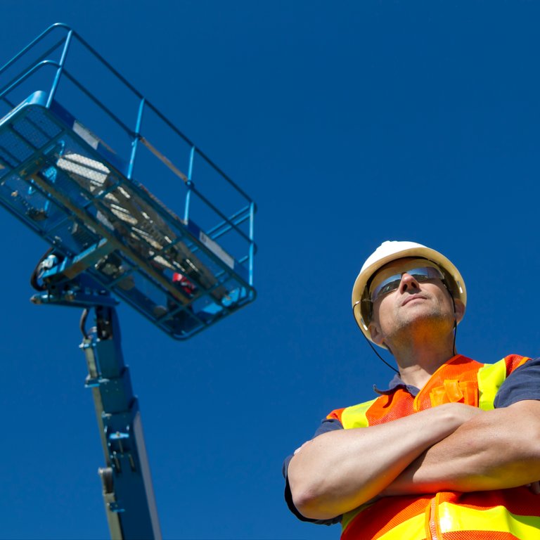 Low angle view of a construction worker and aerial work platform with clear blue sky in the back.