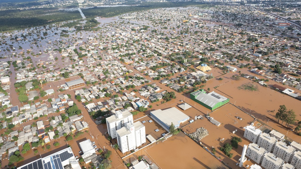 Aerial view of a flooded urban area with submerged houses, streets, and buildings, surrounded by hills in the background.