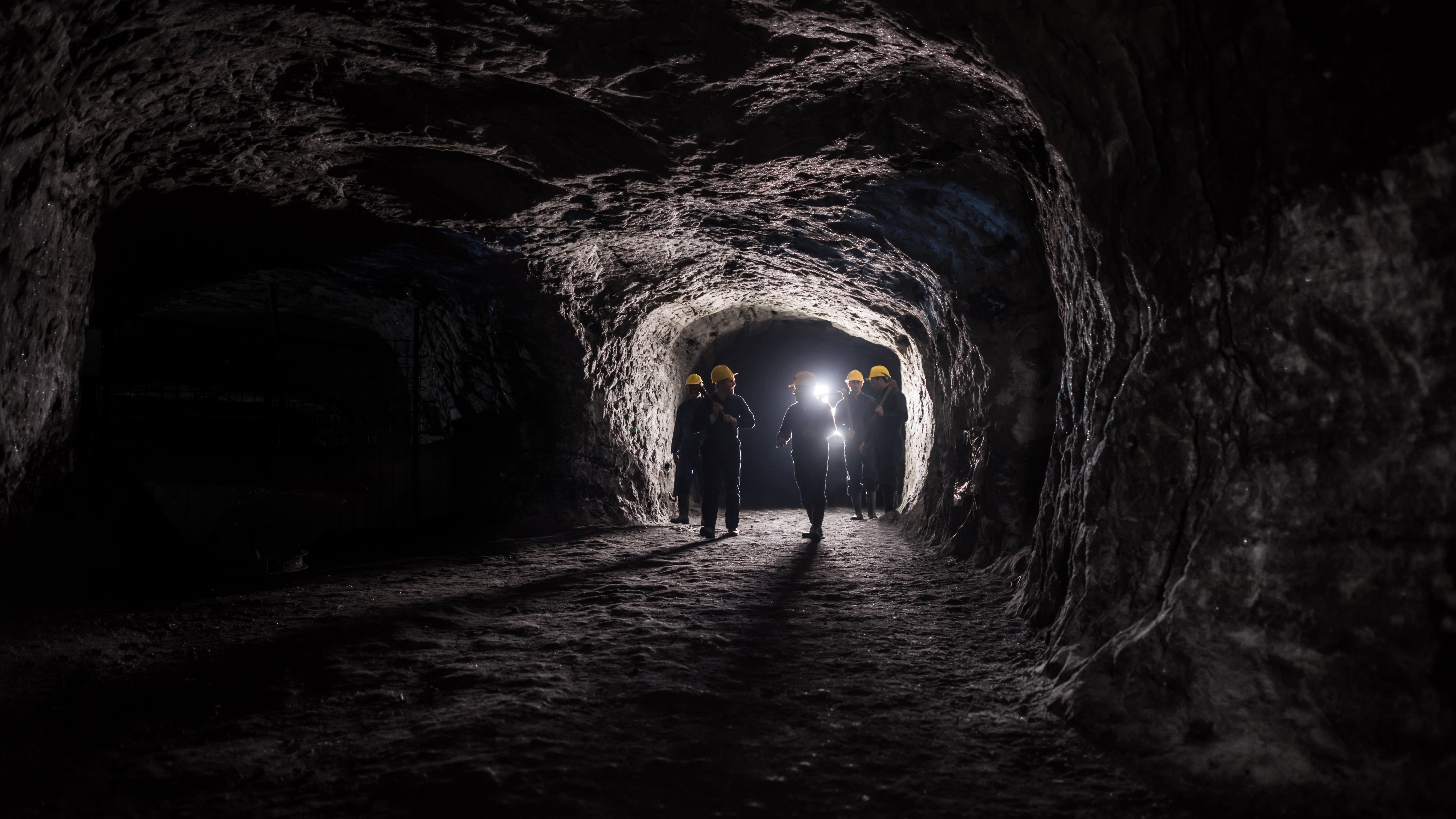Miner Rescue Insurance A group of coal miners walking through a mining shaft of an underground coal mine, bright lights behind them.
