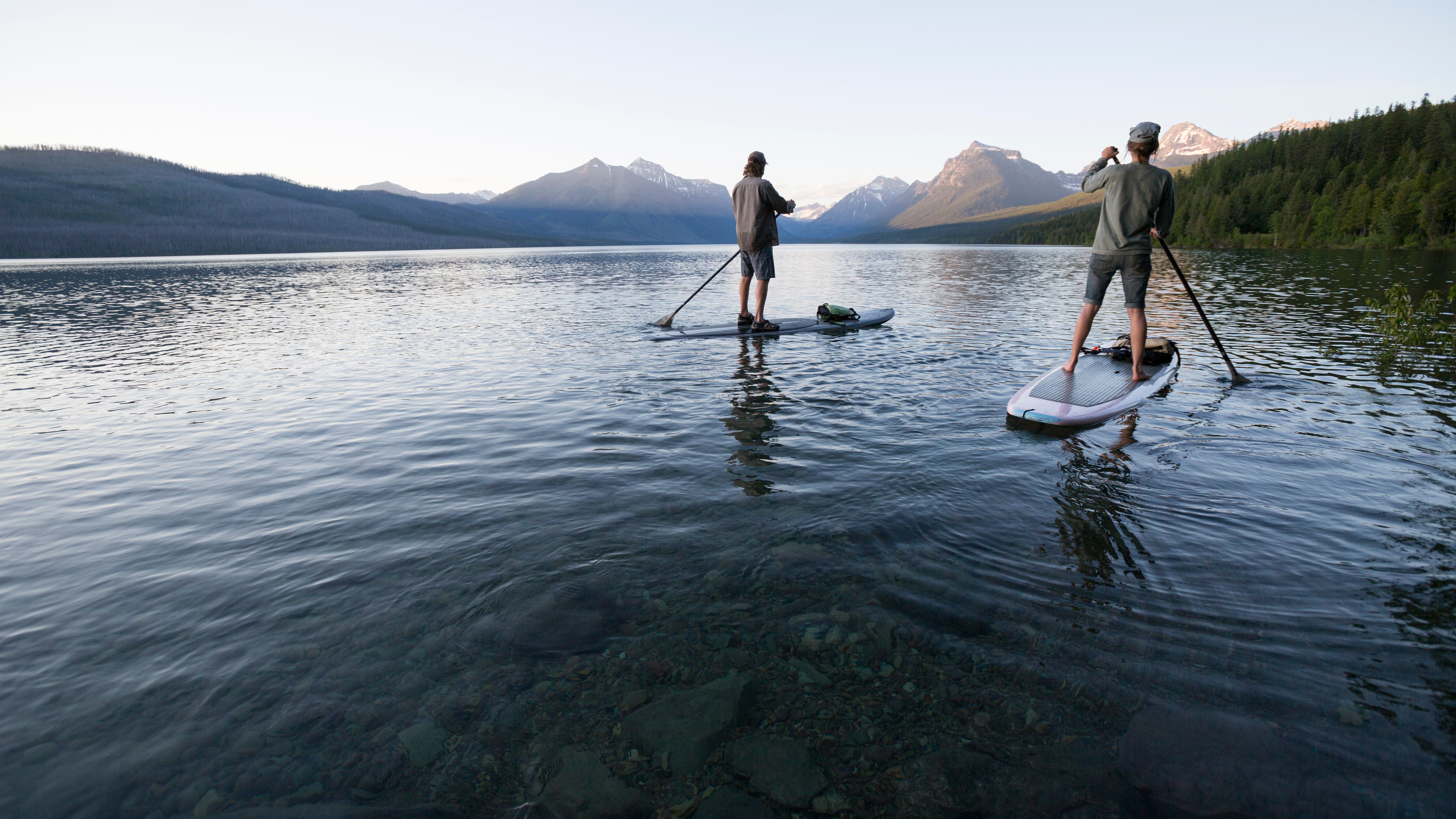 Die Balance aus Risiko und Leistung halten im Motiv zwei SUP-Fahrer vor Bergkulisse