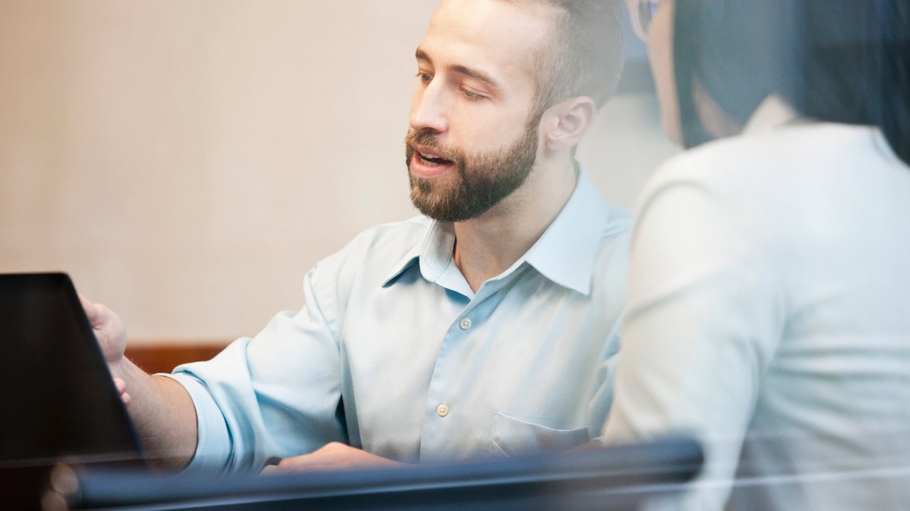 A man in a light blue shirt and a woman in a white shirt are engaged in a discussion at a table.