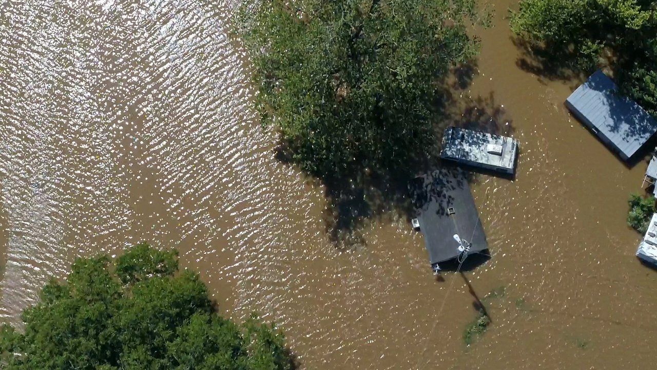 Aerial view of flooded area with submerged houses and trees in brown water.