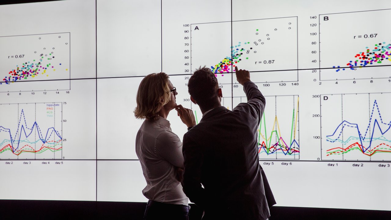 Business men in a dark room standing in front of a large data display of mortality trends in group life