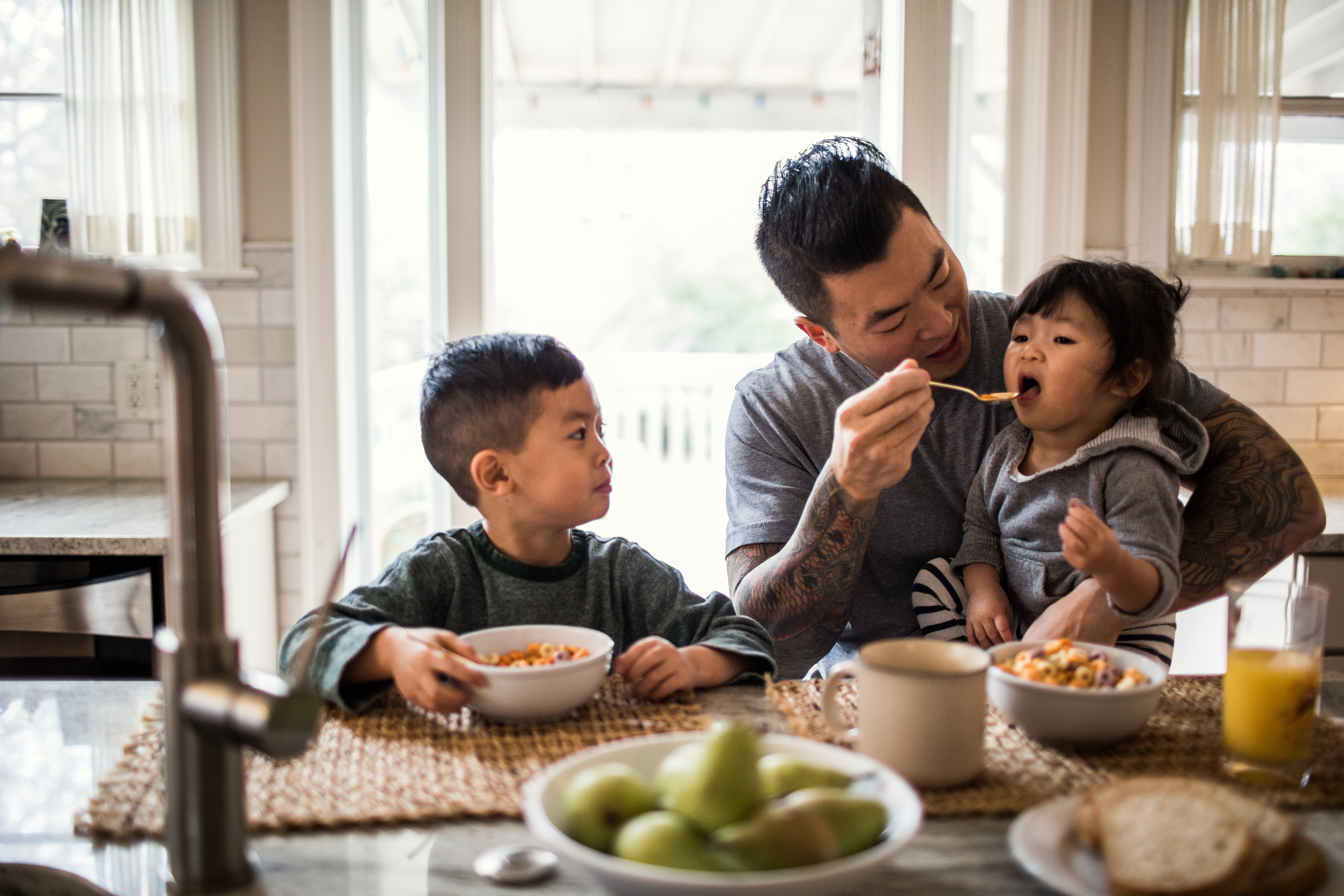 A father feeding his children at the table in their home.