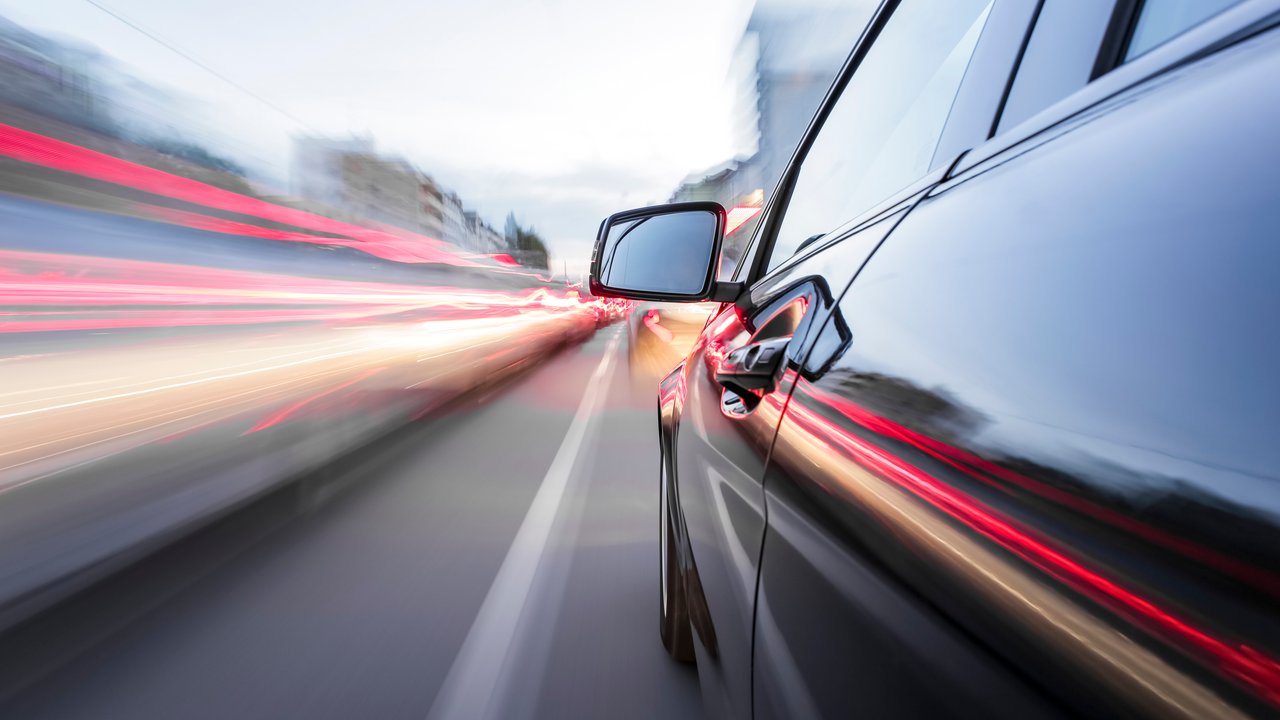 A black car in motion with blurred lights from other vehicles on the road.