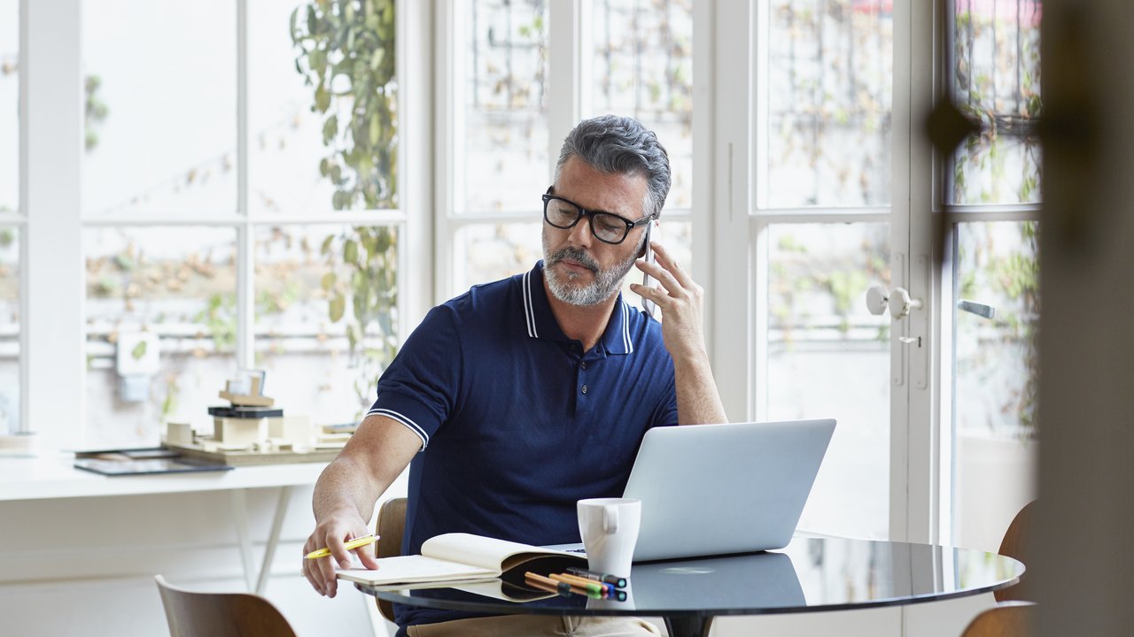 Businessman and mobile phone and laptop writing notes