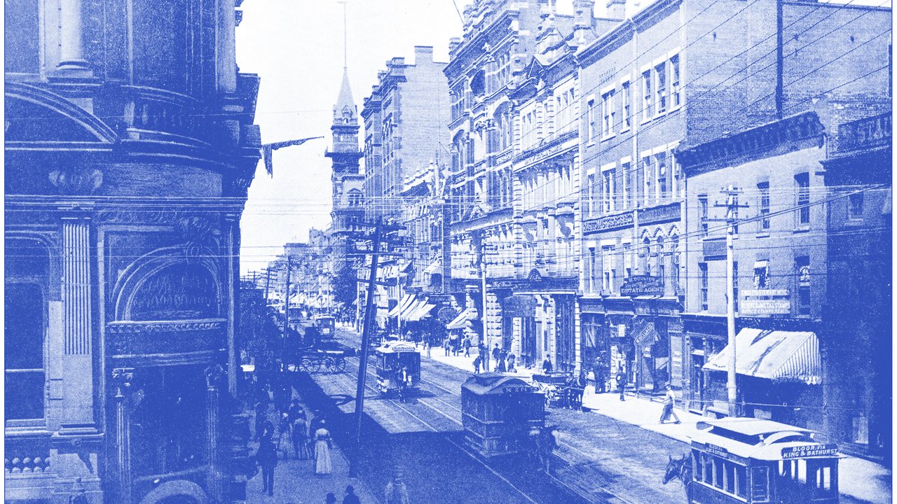 A bustling urban street scene features historic buildings with ornate architecture, some displaying signs for businesses. Streetcars travel along the tracks, while pedestrians stroll on the sidewalks. Flags hang from the buildings, adding a festive touch. The image is rendered in a blue tint, enhancing its vintage feel.
