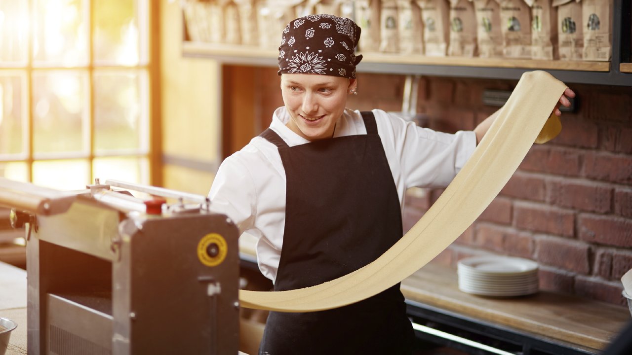 Woman cooks dough on machine for making pasta