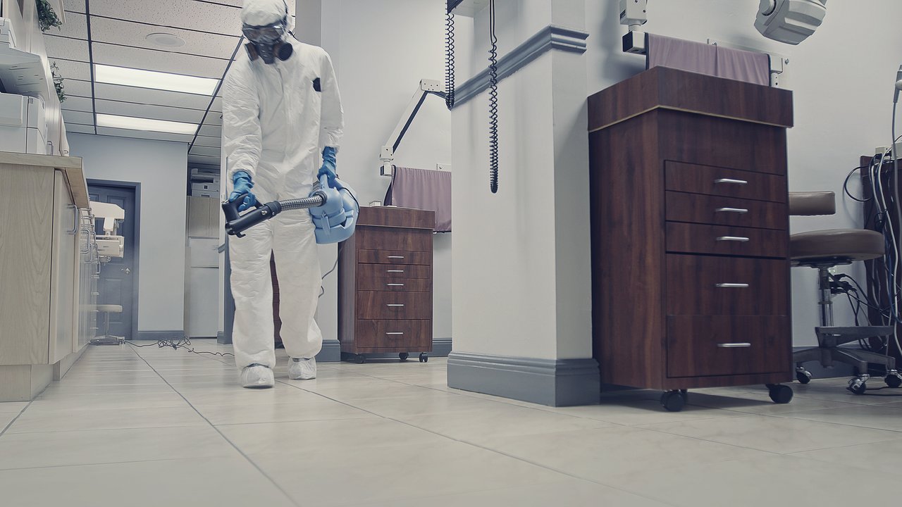 A person fogging with disinfectant, dressed in protective gear, in a dental office