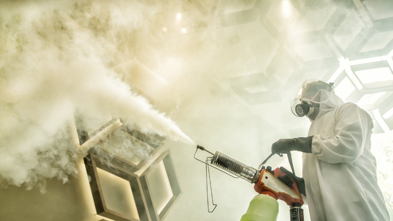 A person excessively fogging with disinfectant, dressed in protective gear