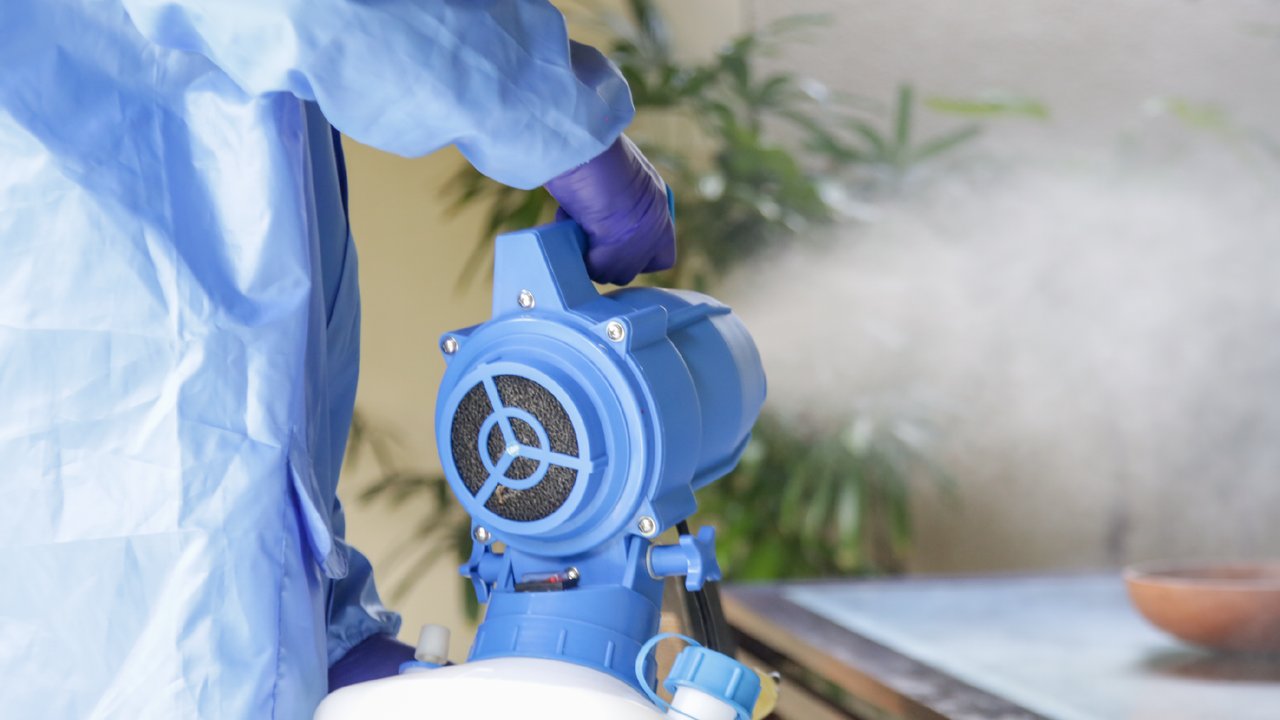 A person fogging with disinfectant, dressed in protective gear