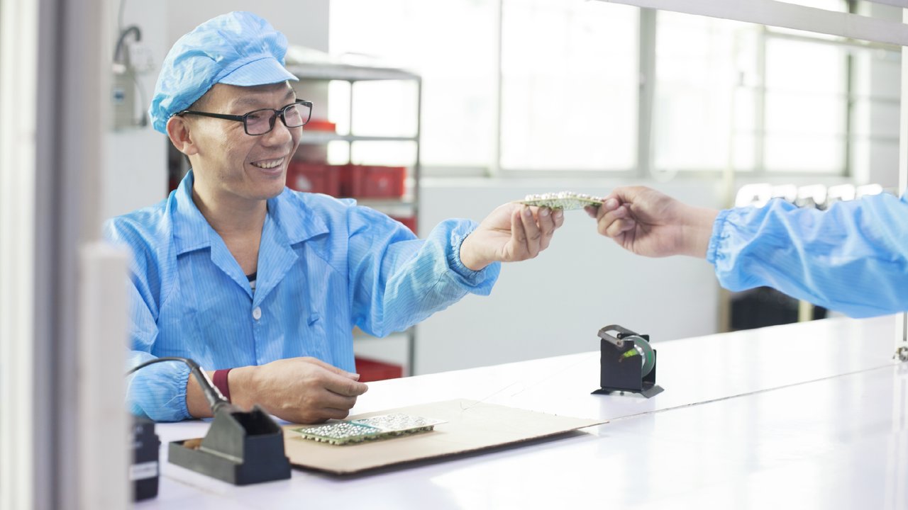 Workers in uniform passing a component in LED lighting factory