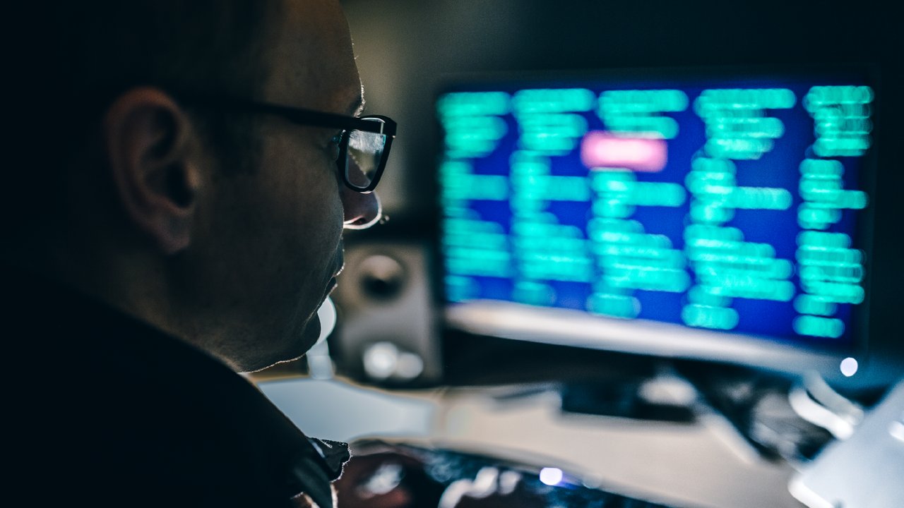Computer hackers wearing glasses and using a computer in a dark room