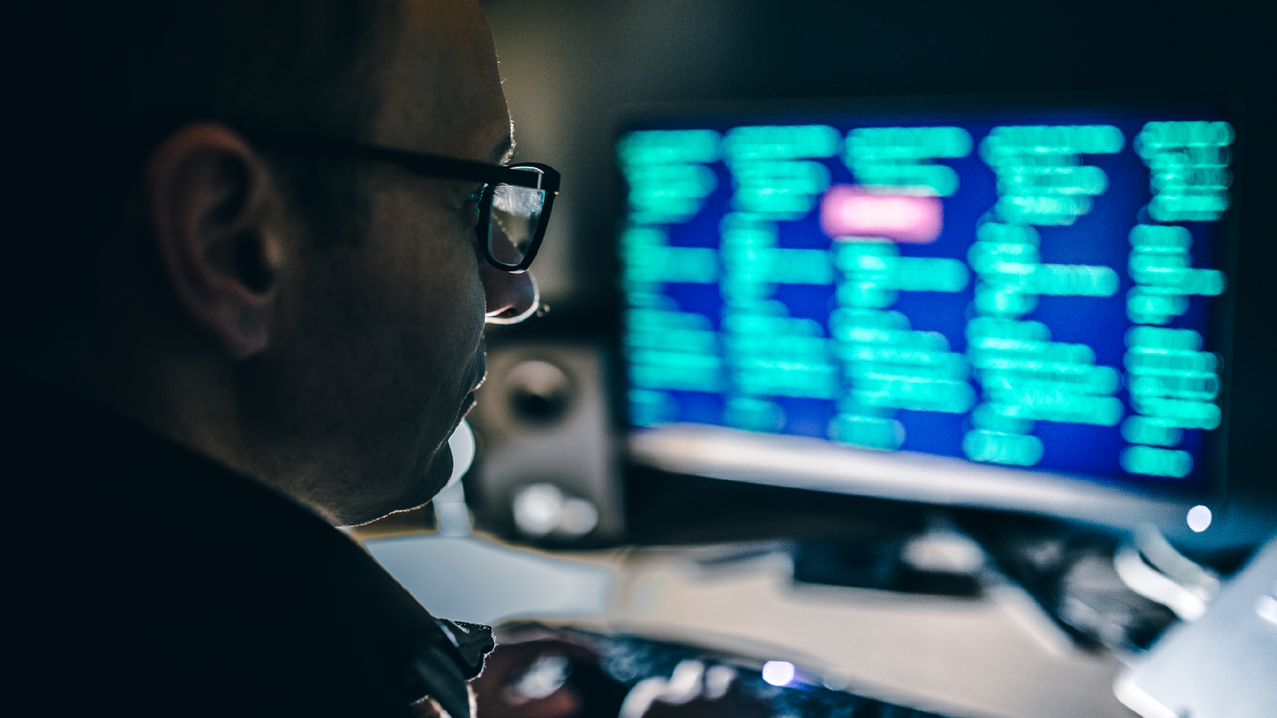 Computer hackers wearing glasses and using a computer in a dark room
