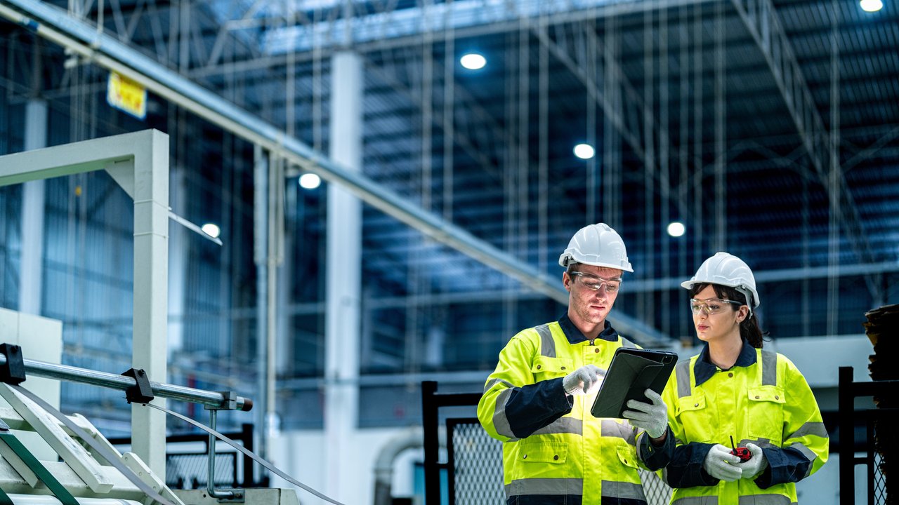Male and female engineers in neat work clothes prepare and control the production system of large modern machines in a factory producing industrial technology products.
