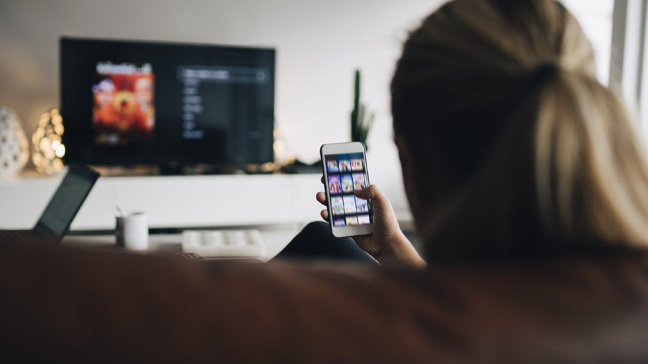 A person sitting on a couch using a smartphone app to control a smart TV in a living room