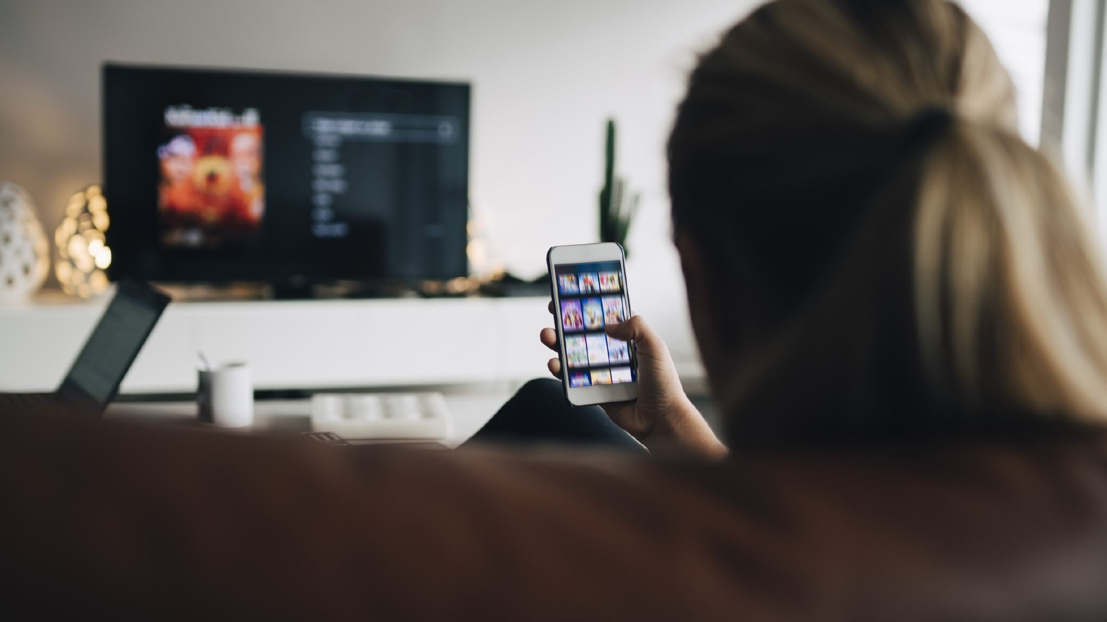 A person sitting on a couch using a smartphone app to control a smart TV in a living room