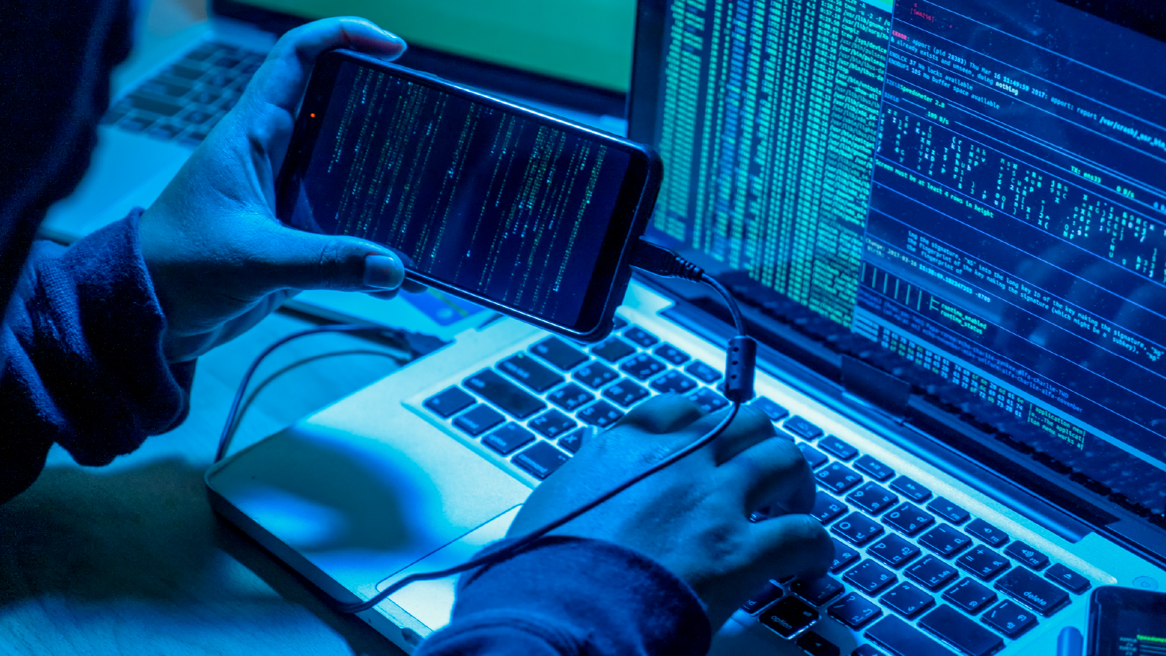 Un pirate informatique avec des ordinateurs et un téléphone intelligent dans une pièce sombre commettant un cyber-crime