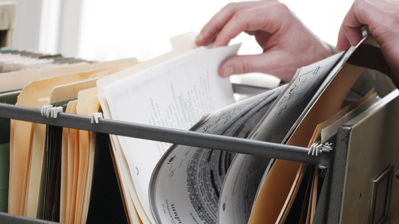 A hand of a person sorting through files stored in a filing cabinet