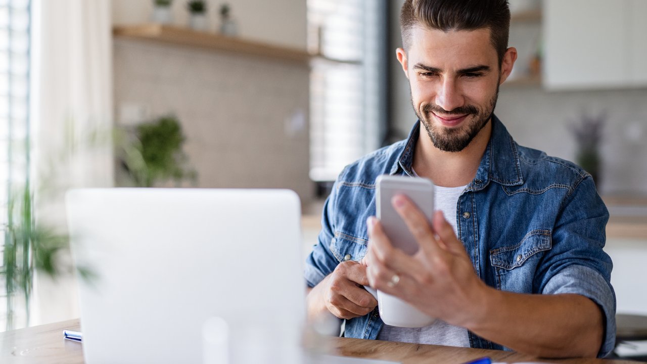 A person sitting at a desk working, using a laptop and smartphone