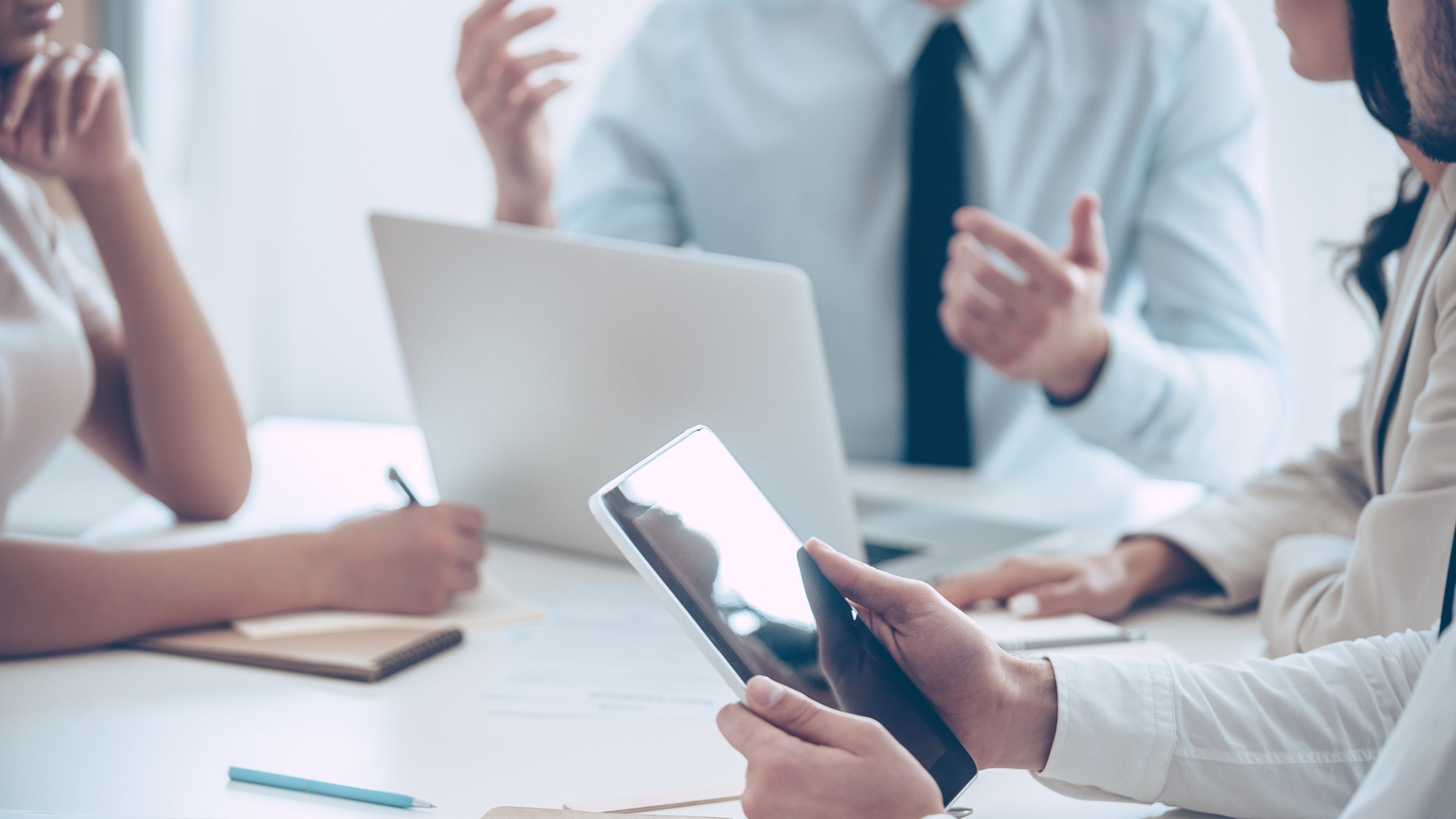 Colleagues having an in person meeting, using a tablet, a laptop, and a notebook