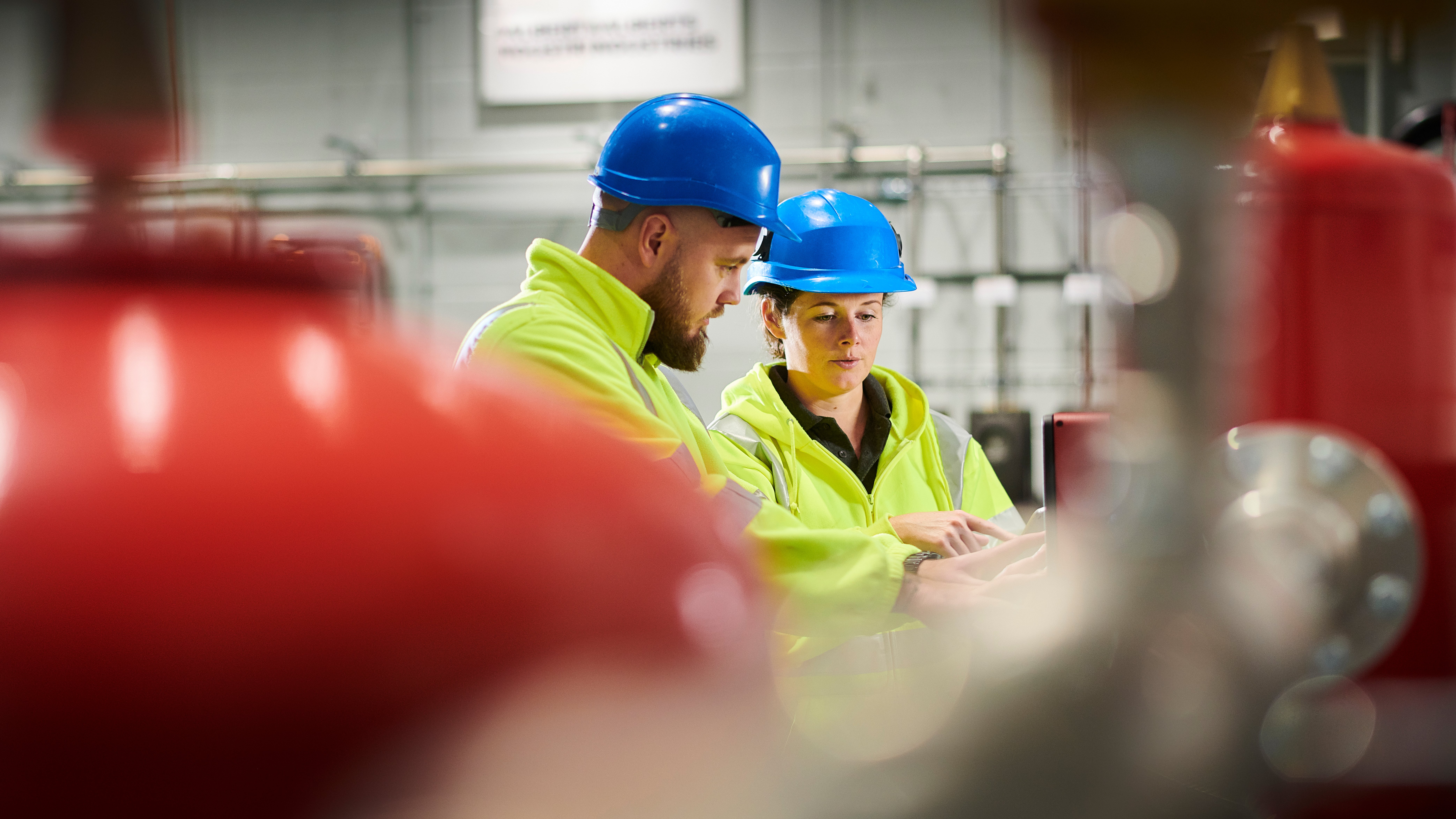 A man and a woman engineers in turbine room with protective gear, looking at machinery